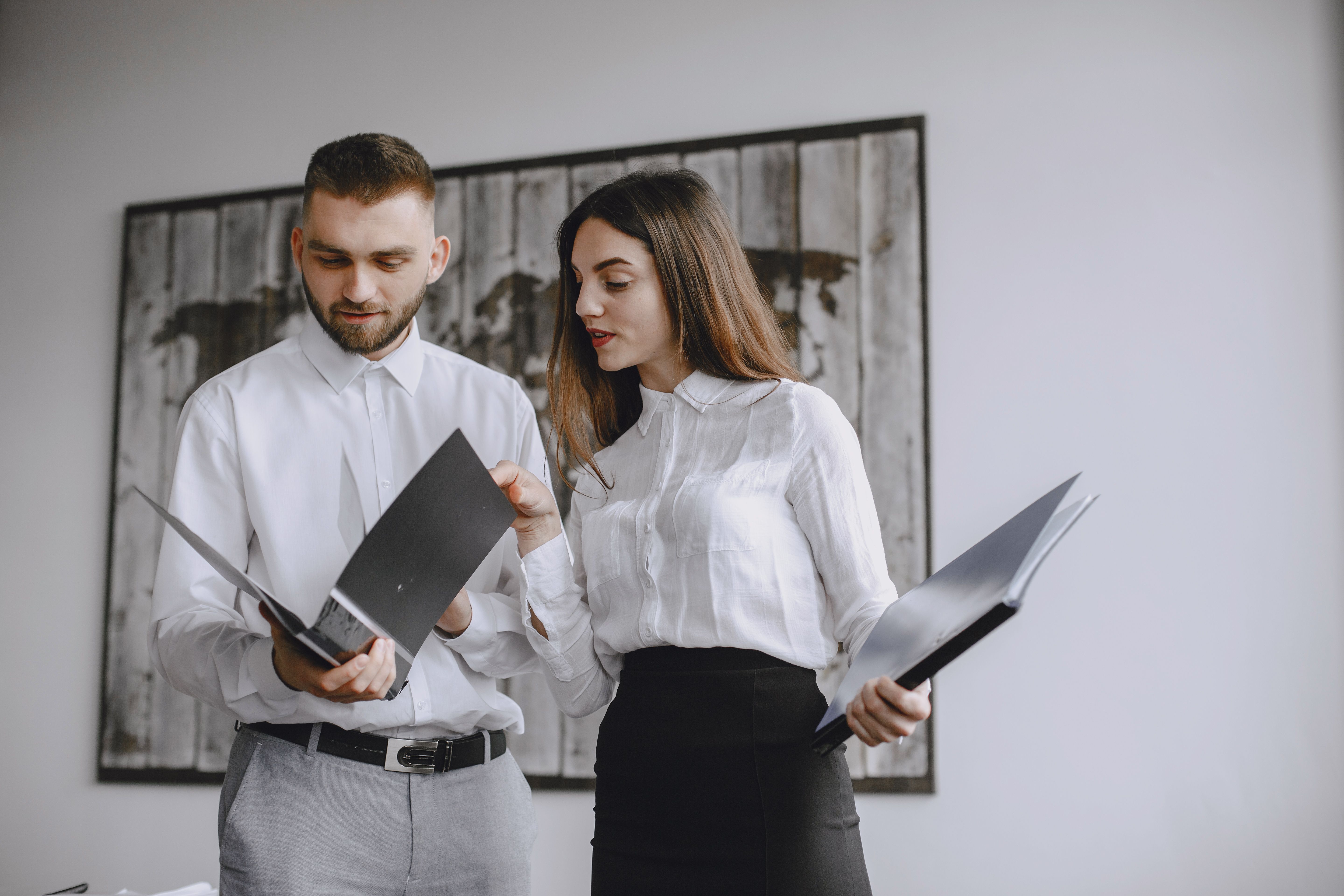 Two colleagues reviewing folders and documents together in an office.